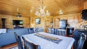 Interior de una cabaña de madera con comedor, cocina y una gran lámpara de araña.