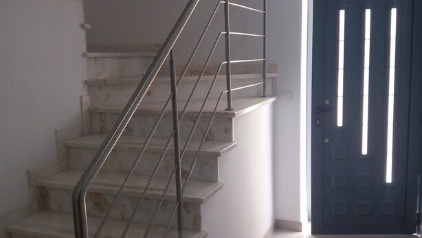 A staircase with metal railings leading to a landing, a dark door with vertical slits, and a small rug on the floor. - Alojamento dos Redondos (Fernão Ferro)