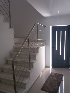 A staircase with metal railings leading to a landing, a dark door with vertical slits, and a small rug on the floor. - Alojamento dos Redondos (Fernão Ferro)