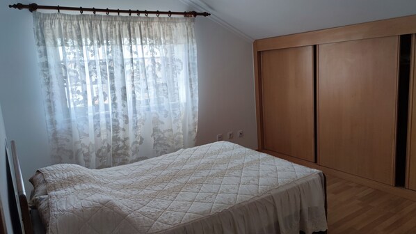 A bedroom with a bed, a window with sheer curtains, and a wooden wardrobe. - Alojamento dos Redondos (Fernão Ferro)