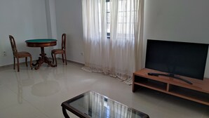 A living room with a wooden TV stand, a glass coffee table, a round wooden table with two chairs, and sheer curtains. - Alojamento dos Redondos (Fernão Ferro)