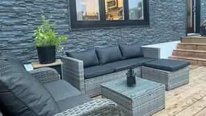 Ein moderner Außenbereich mit Sitzgelegenheiten, einer Steinwand im Hintergrund, einer Couch, zwei Hocker und einem kleinen Tisch.