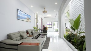 A modern living room with a sectional sofa, a coffee table, and a large window with plants. - NatalieLe's Homestay (Phu Quoc)