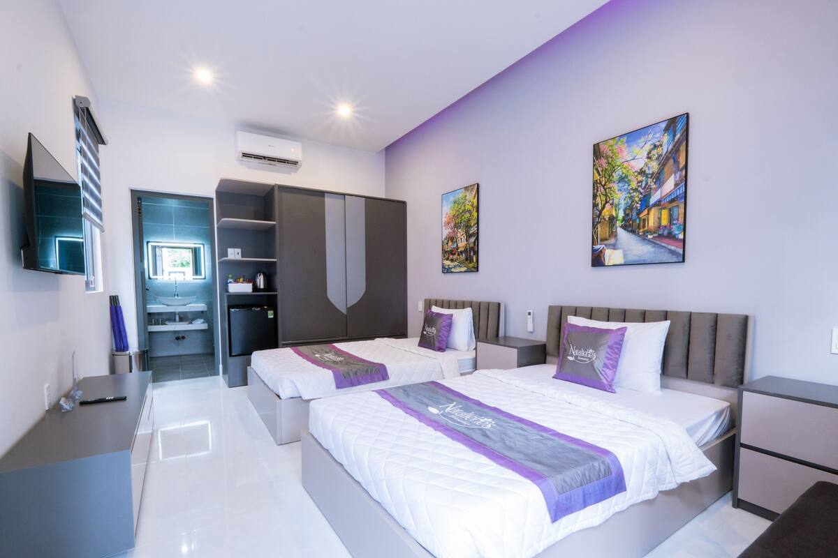A modern hotel room with two beds, a bathroom, a desk, and a TV.