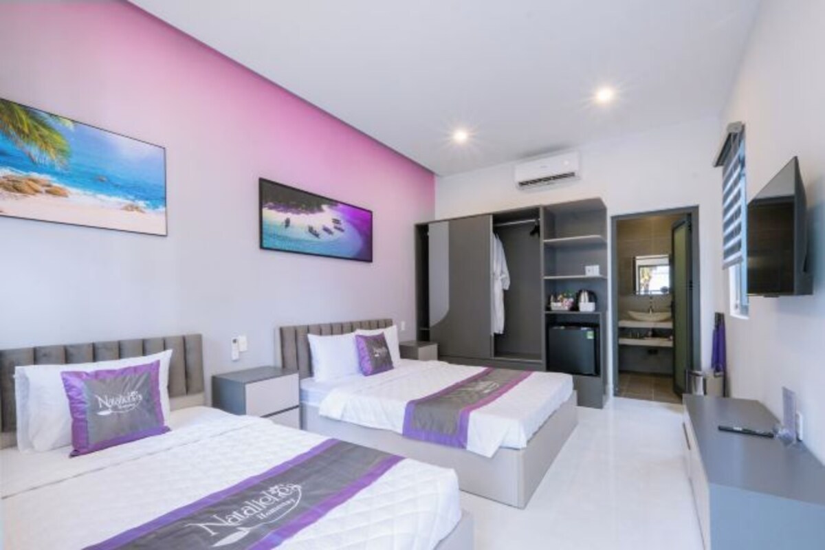 A hotel room with two beds, a wardrobe, a TV, and artwork on the walls.