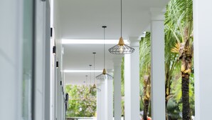 A corridor with hanging pendant lights, white columns, and a view of greenery outside. - NatalieLe's Homestay (Phu Quoc)