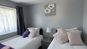Habitación de hotel con dos camas, una mesita de noche, una lámpara y un ventanal con cortinas.