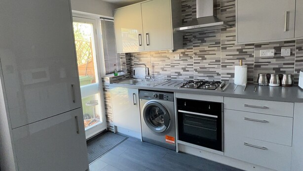 Una cocina moderna con lavadora y secadora integradas, electrodomésticos de acero inoxidable y un salpicadero de azulejos.