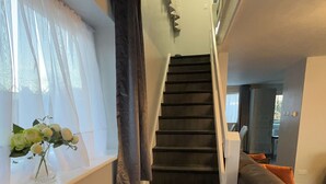 Una escalera que conduce a un segundo piso, con un ventanal en la barandilla y un jarrón de flores en la pared.