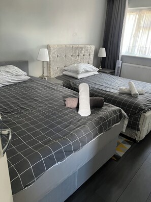 Une chambre d’hôtel avec deux lits, une tête de lit, des lampes de chevet, un radiateur et une fenêtre avec des rideaux.