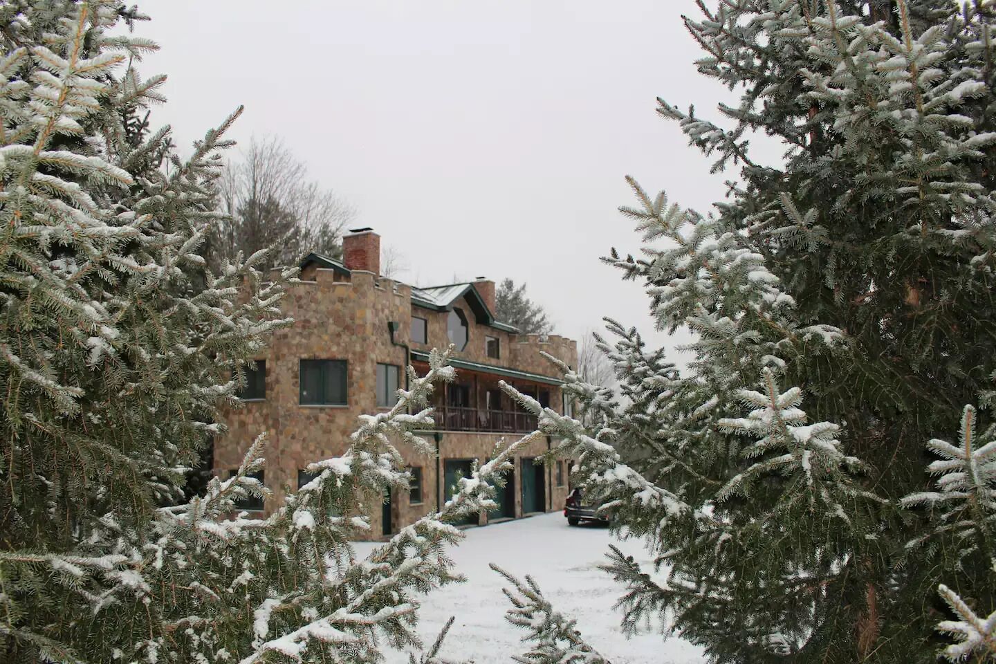 Un bâtiment en pierre doté de nombreuses fenêtres et d’un balcon, entouré d’arbres couverts de neige.