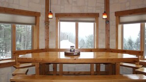 Ein Holzesstisch mit Bänken, große Fenster und hängende Pendelleuchten in einem raum im Blockhausstil.