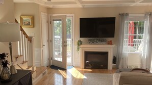A spacious living room with hardwood flooring, a fireplace, a television, and a sofa.
