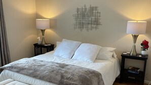 A neatly arranged bedroom with a large bed, two bedside tables with lamps, a decorative wall piece, and a wooden floor.