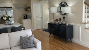 A modern living room with a sofa, coffee table, and a dining area with a refrigerator and coffee machine.