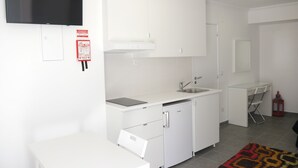 Une cuisine moderne avec des meubles blancs, un lave-vaisselle encastré, un évier et un téléviseur à écran plat fixé au-dessus du plan de travail.