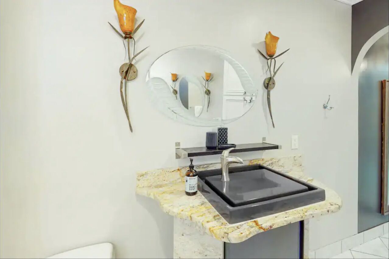 Une salle de bain avec un lavabo en marbre, un miroir rond et deux appliques murales.
