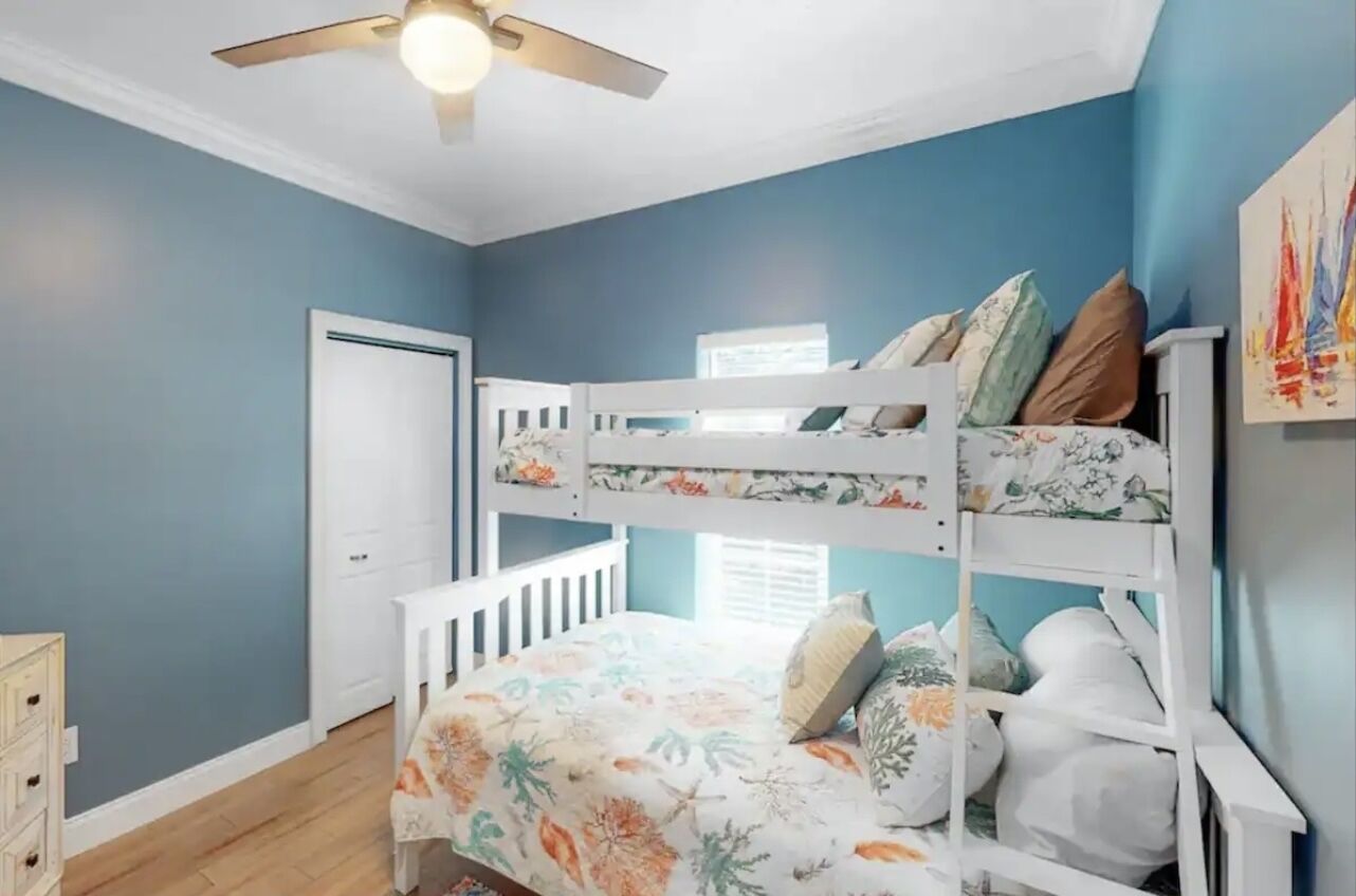 A room with a bunk bed, a ceiling fan, a door, and a window.