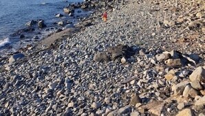 Ein felsiger Strand, eine Person geht vom Betrachter weg.