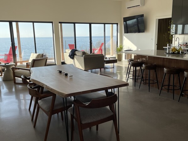 Una cocina moderna con una isla grande, un comedor con mesa y sillas de madera, y amplias ventanas con vistas al mar.