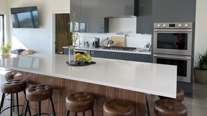 Eine moderne Küche mit einer großen Kochinsel, Barhocker, einem eingebauten Ofen und einem an der Wand befestigten Fernseher.