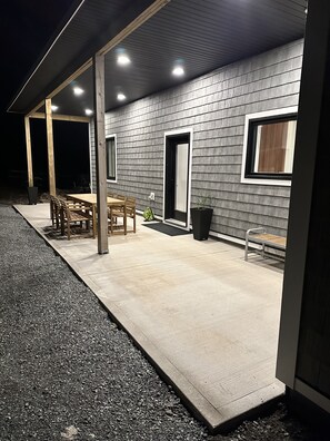 Un espacio al aire libre techado, con suelo de hormigón, mobiliario de madera y pared de ladrillo gris.