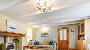 A cozy living room with a fireplace, a sofa, a wooden cabinet, and a chandelier. - Wedgwood Cottage - Sleeps 6 guests  in 3 bedrooms (Cawsand)