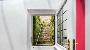 A white door with a glass panel, leading to a stone staircase surrounded by greenery. - Wedgwood Cottage - Sleeps 6 guests  in 3 bedrooms (Cawsand)