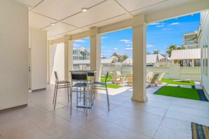 A spacious patio area with a table and chairs, a small lawn, and a view of neighboring houses. - 3-story ocean-view home with pool, grill, golf, gym, pool table, & washer/dryer (Port Aransas)