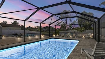 An outdoor swimming pool with a glass enclosure, surrounded by lounge chairs and a patio area.