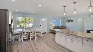 A modern kitchen with white cabinets, a stainless steel refrigerator, and a dining area with a white table and chairs. - CLEAN,Great Location,Dockage Available,HEATED Pool,3 Units, HUGE Back yard.Apt A (Englewood)