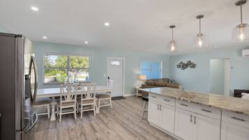 A modern kitchen with white cabinets, a stainless steel refrigerator, and a dining area with a white table and chairs.