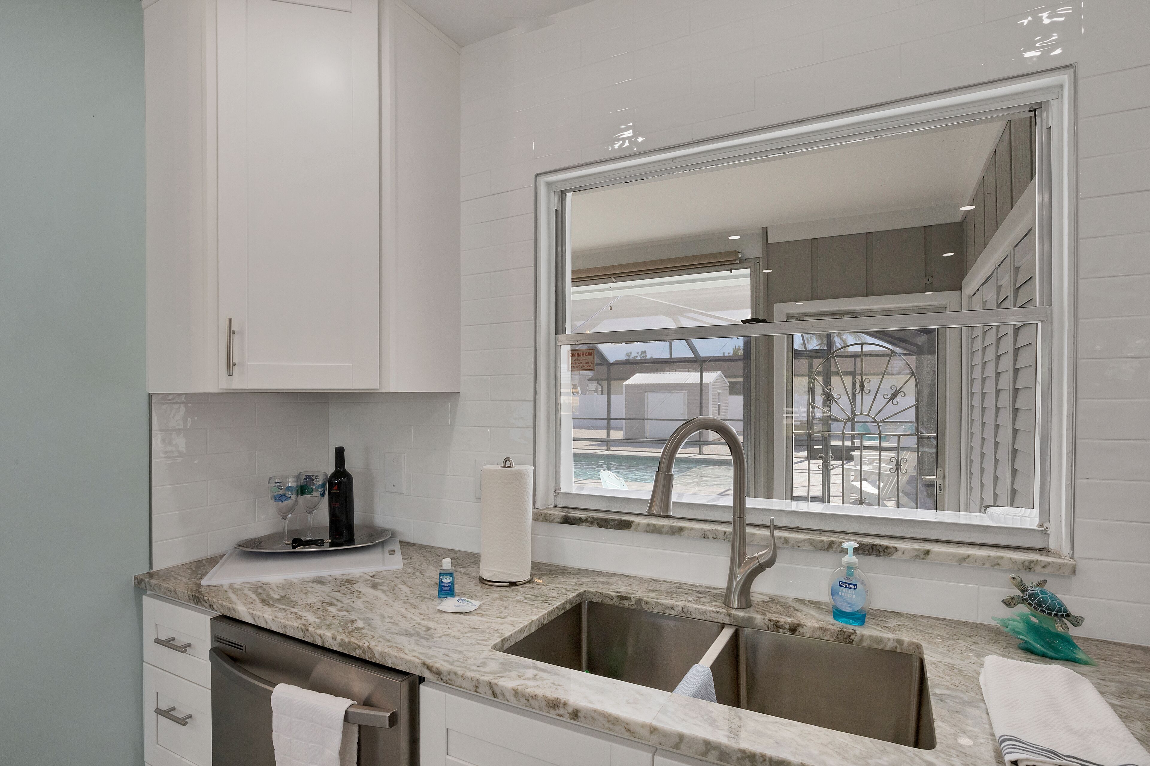 A kitchen with white cabinets, a marble countertop, a stainless steel sink, and a window with a view of a balcony.