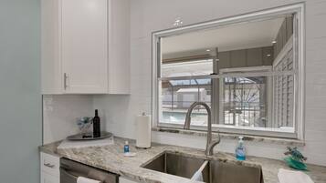 A kitchen with white cabinets, a marble countertop, a stainless steel sink, and a window with a view of a balcony.