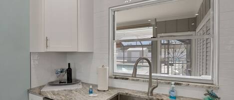 A kitchen with white cabinets, a marble countertop, a stainless steel sink, and a window with a view of a balcony.