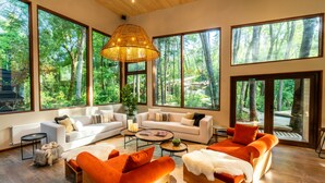 A spacious living room with large windows, a white sofa, orange sofas, and a wooden coffee table. - rakau lodge (Pucón)