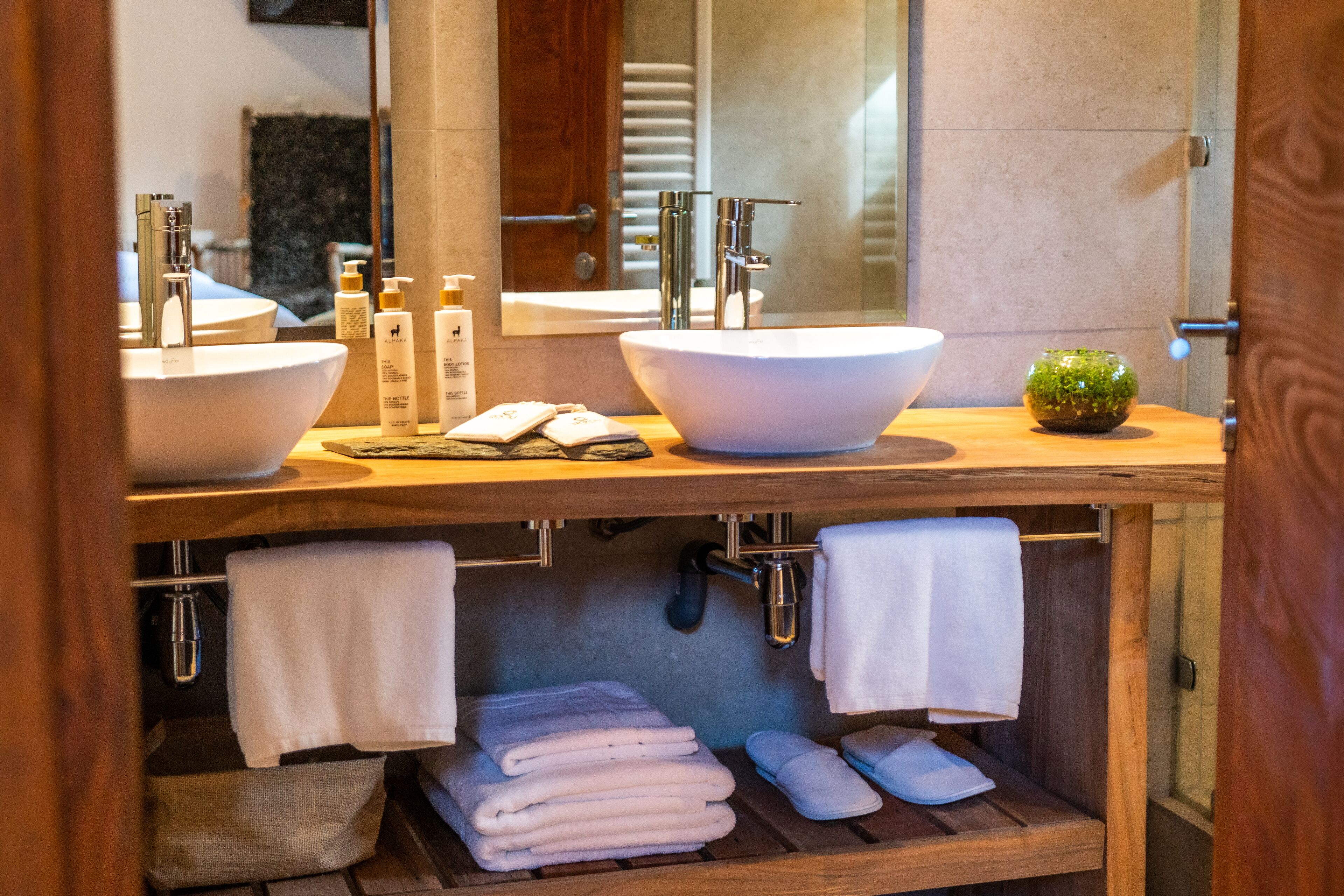 Un baño con dos lavamanos grandes, un espejo y un mueble de tocador de madera con toallas y artículos de aseo.
