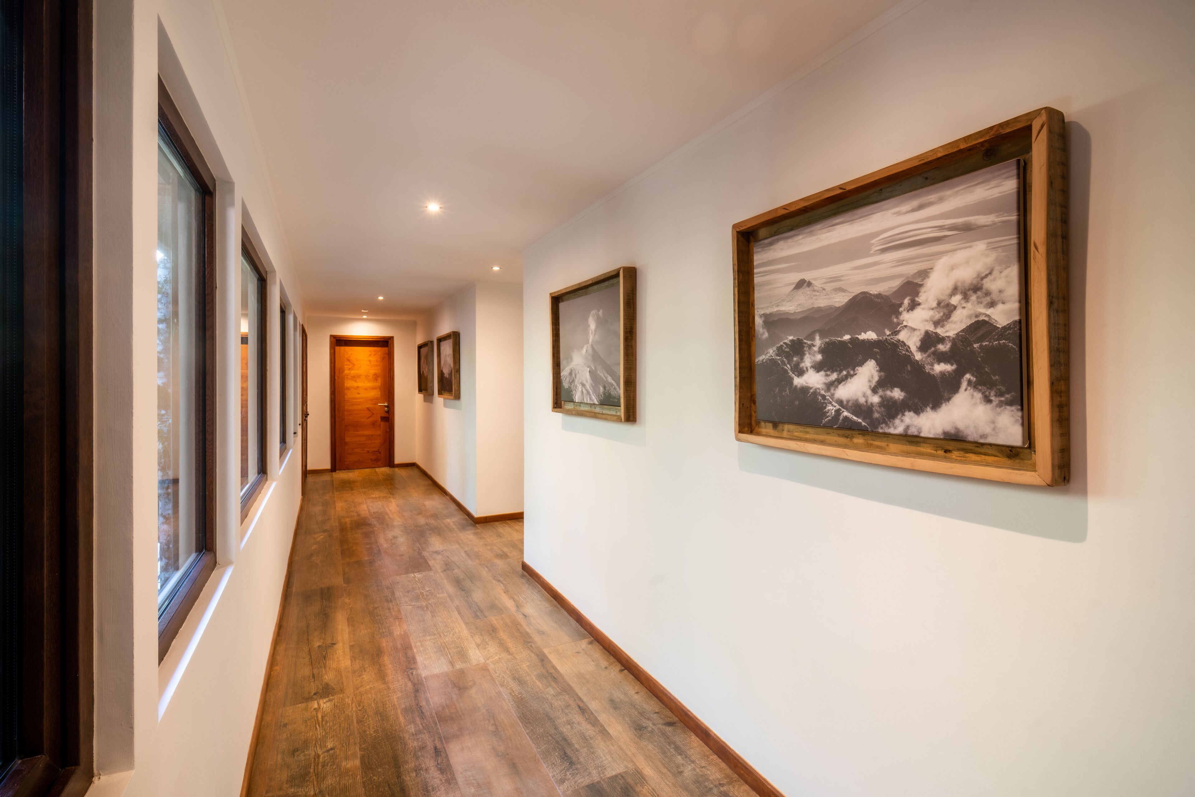 A hallway with wooden flooring, framed pictures on the walls, and a wooden door at the end.