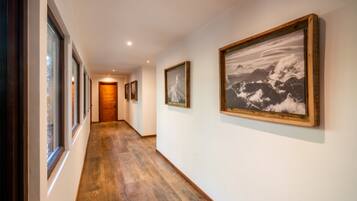 A hallway with wooden flooring, framed pictures on the walls, and a wooden door at the end.