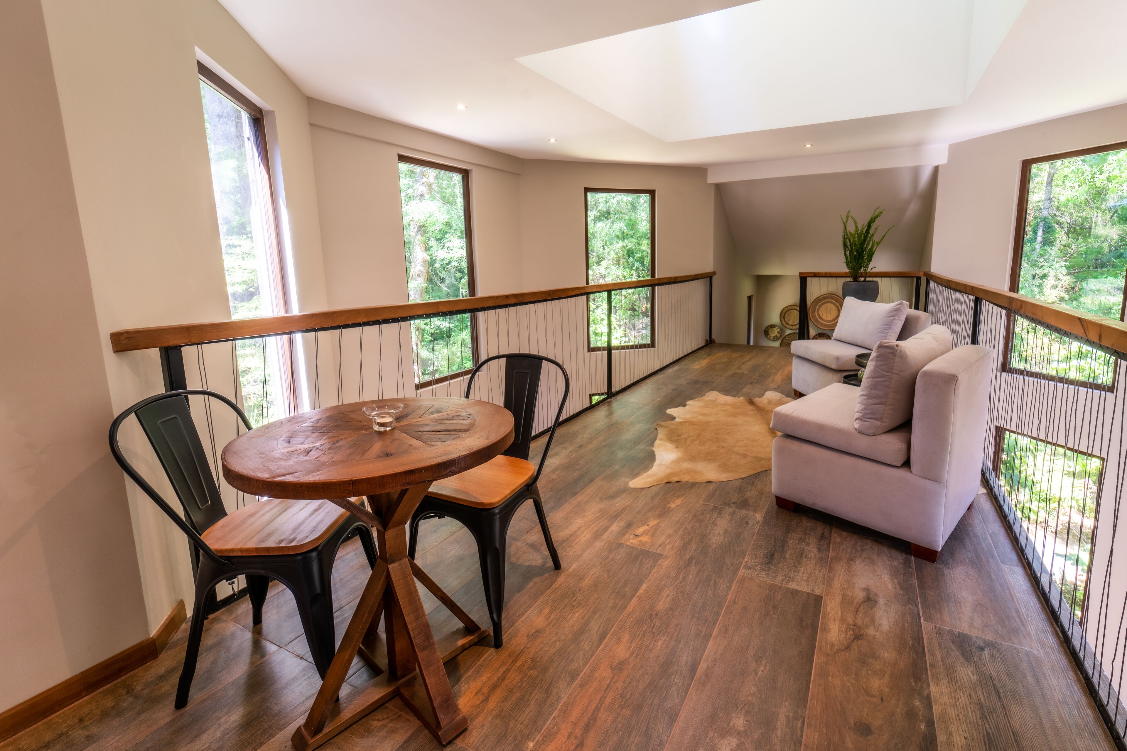 A spacious balcony with a wooden table and chairs, a sofa, and a view of greenery.