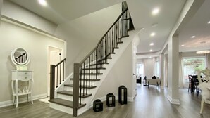 A modern interior with a wooden staircase, a white console table with a mirror, and a dining area with a white sofa and table. - Waterfront Paradise Estate (Aurora)