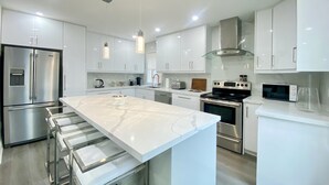 A modern kitchen with white cabinetry, stainless steel appliances, and a marble island. - Waterfront Paradise Estate (Aurora)