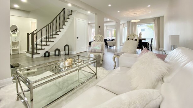 A modern living room with a glass coffee table, white sofa, and a staircase leading to another level. - Waterfront Paradise Estate (Aurora)