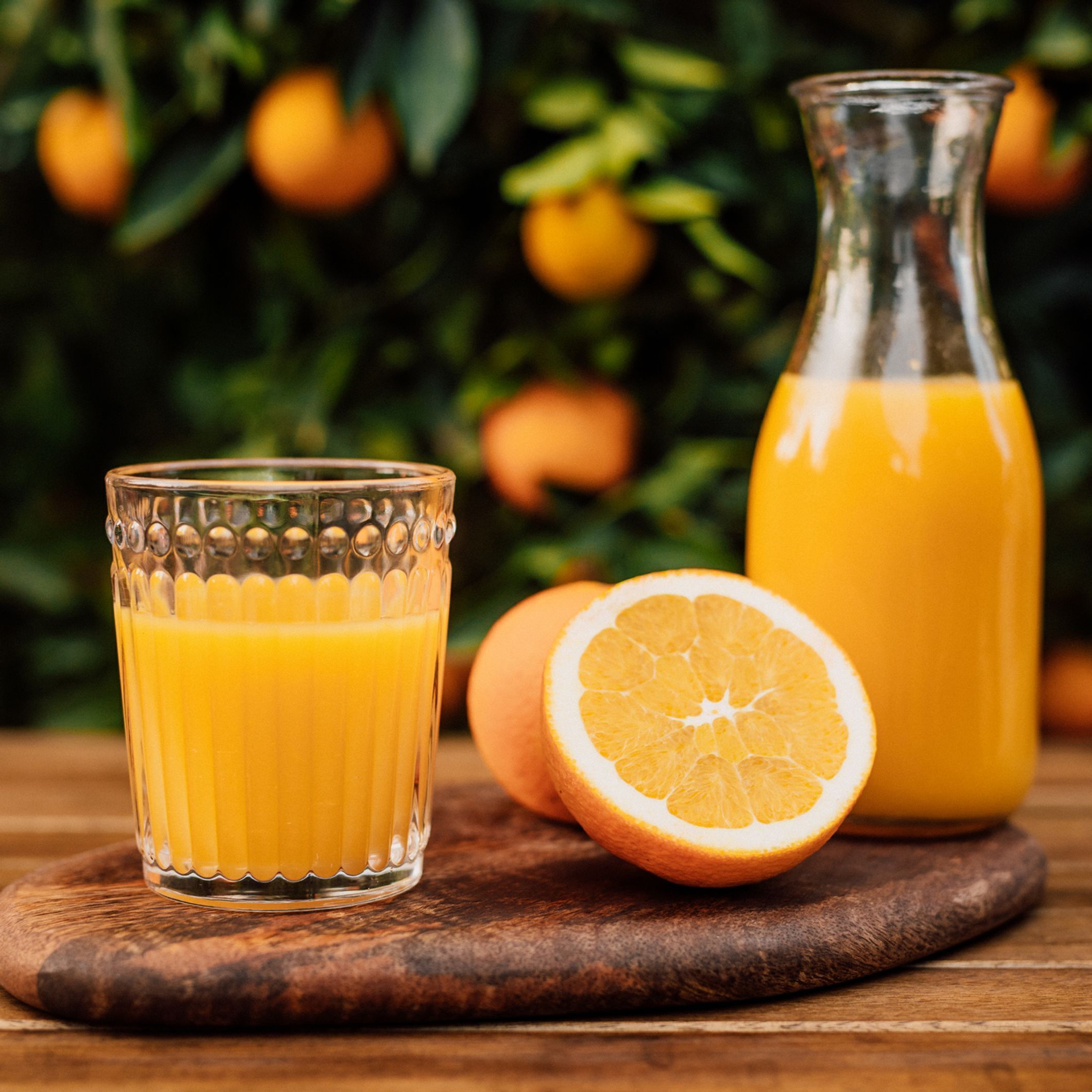 A glass of orange juice, a half orange, and a bottle of orange juice on a wooden surface with oranges in the background.