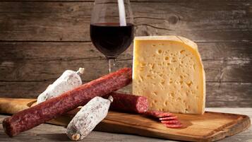 Une planche à découper en bois, sur laquelle on a disposé une grosse tranche de fromage, plusieurs tranches de salami et un verre de vin rouge.