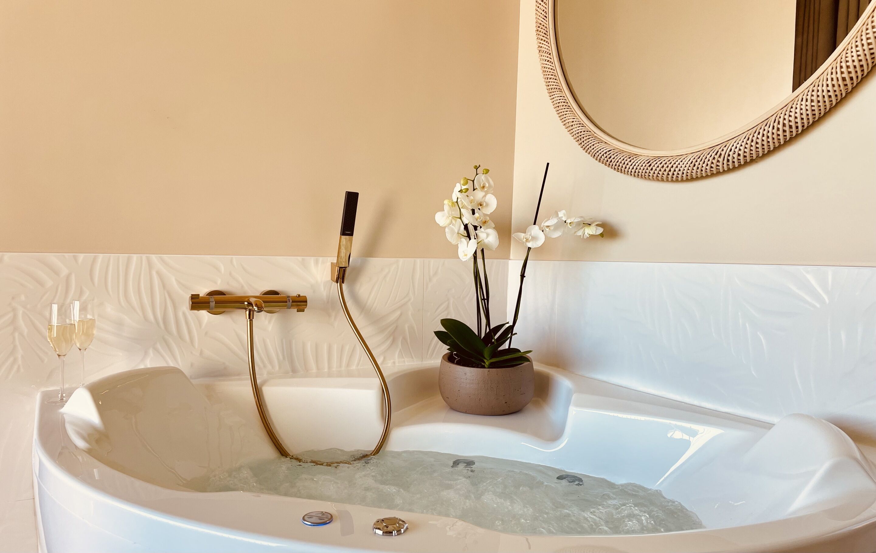 Una bañera con un grifo dorado, una orquídea en maceta y un espejo encima.