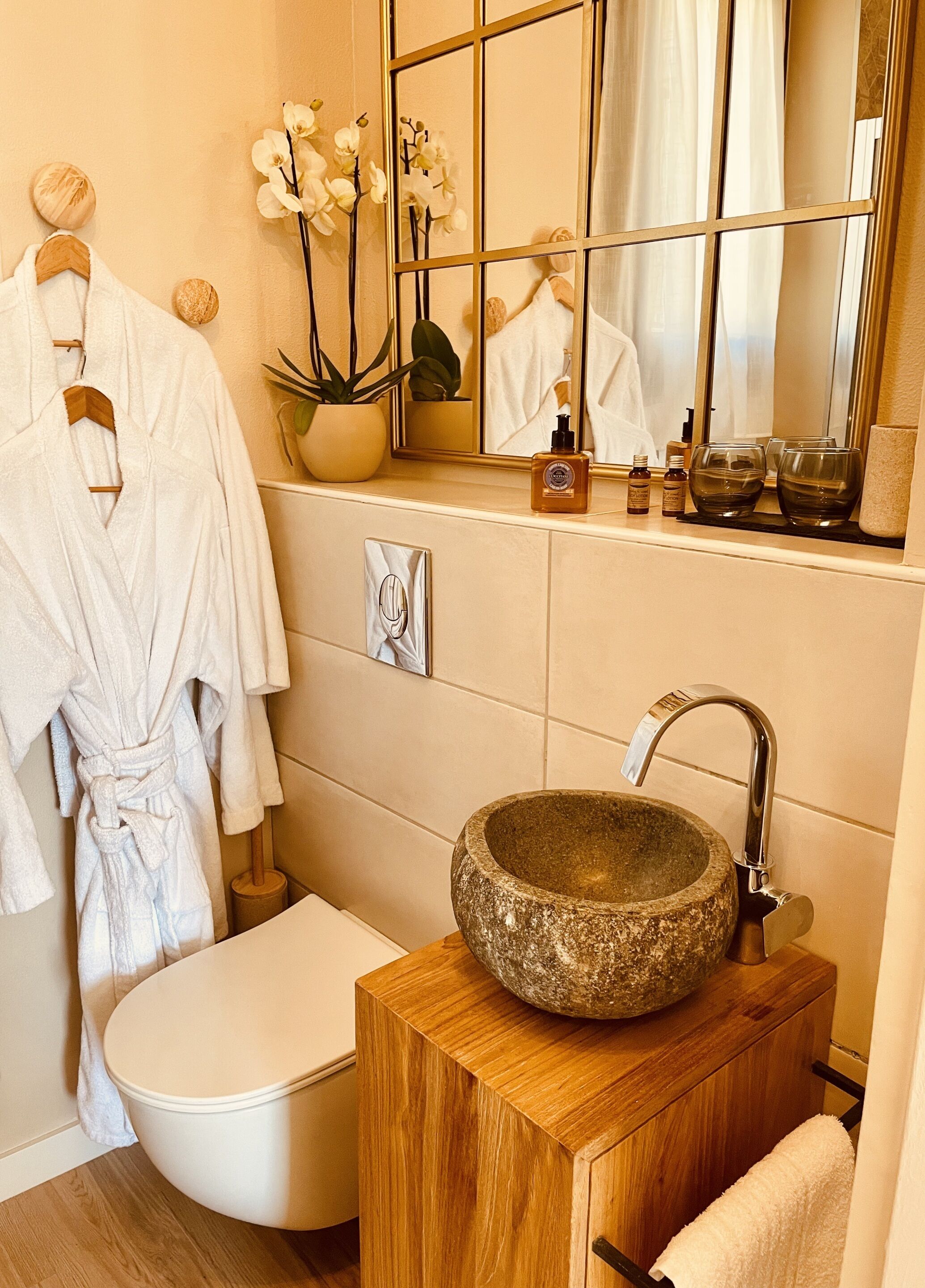 Un baño con un lavabo de piedra, tocador de madera y un inodoro. Hay toallas blancas colgadas en un perchero y un espejo sobre el lavabo.