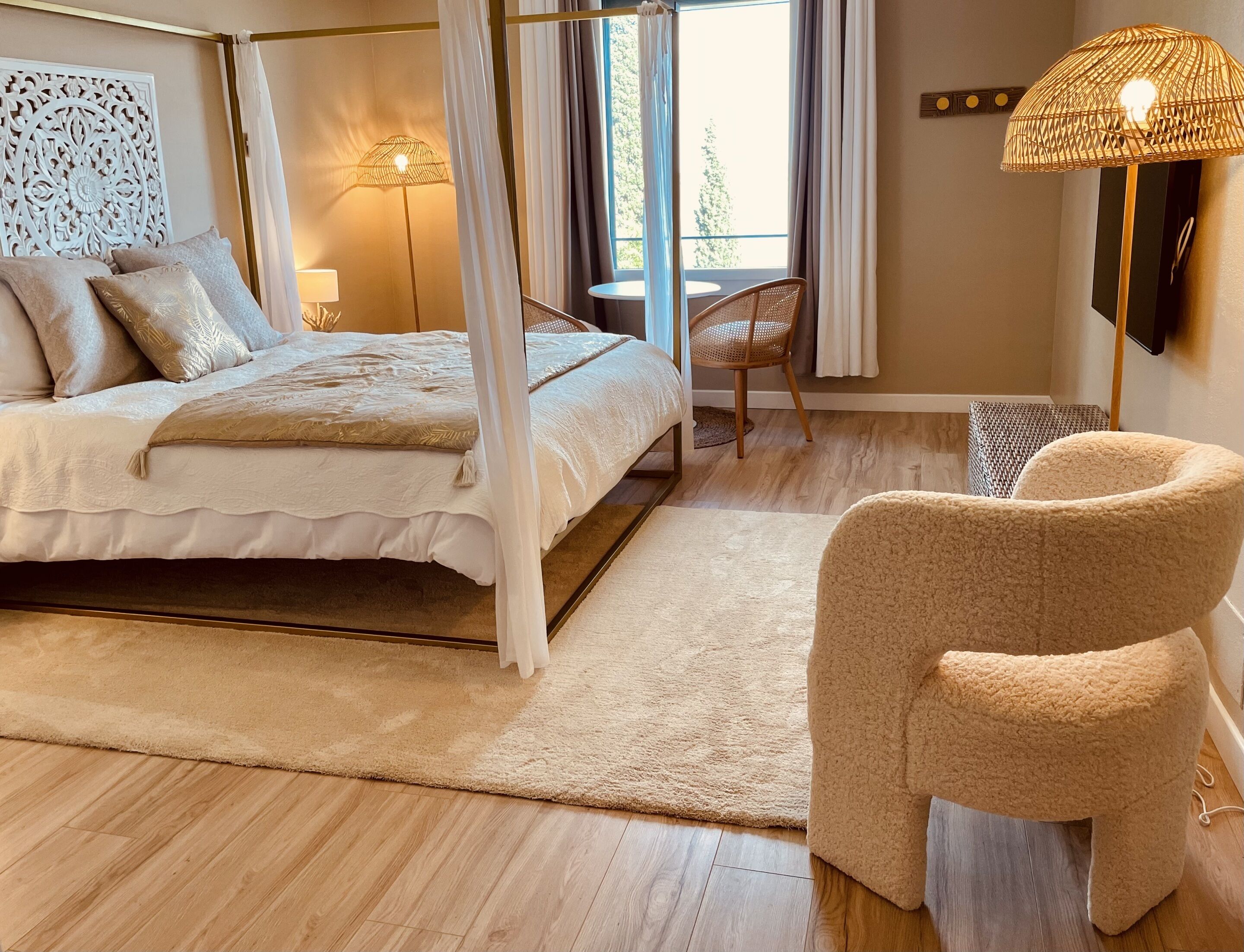 A bedroom with a bed, a chair, a bedside table, a lamp, and a window with curtains.