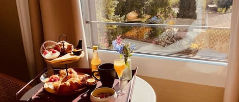 A breakfast tray with croissants, yogurt, and juice on a table by a window with a view of trees and a body of water.