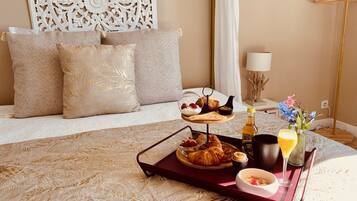 A neatly arranged breakfast tray on a bed with a decorative headboard, a bedside lamp, and a vase of flowers.
